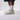 Ett par fötter som bär vita strumpor och Ett par veganska MoEa GEN 9 Corn Pure White Grained sneakers, Skorna är helvita med perforeringar över tån för ventilation, vita, breda skosnörena. Skornas plös, sida och hälkappa har varumärkets namn i svart text.