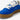 En detaljbild på en vegansk, MoEa GEN 9 Mushroom Full Blue Suede sneaker. Skorna har en blå mockaöverdel med perforeringar över tån. Kontrasterande vita detaljer syns vid sidan och längs snörningen, vita, tjocka skosnörena. Skons plös är vit med en vit etikett med svart text med varumärkets namn, vit hälkappa. Sulorna är i en ljusbrun, gummiaktig textur. Skorna utstrålar en modern och medveten stil. Bilden är mest fokuserad på snörningen. 