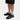 En person klädd i Virón svarta sneakers modell 2005, svarta shorts och gråa strumpor, inzommad på skorna.